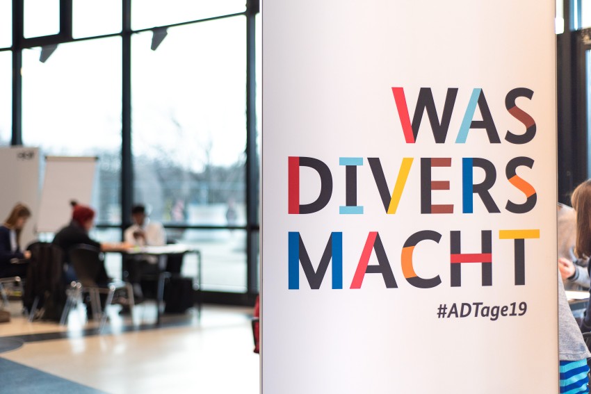 Poster im Vordergrund mit Aufschrift "Was divers macht!"