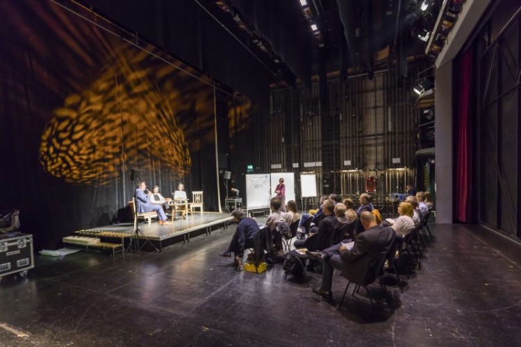 Saal mit Zuschauern und einer Bühne mit einem Podium