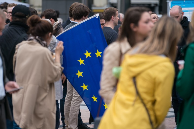Eine Gruppe von Menschen, eine Person hält eine Flagge der Europäischen Union