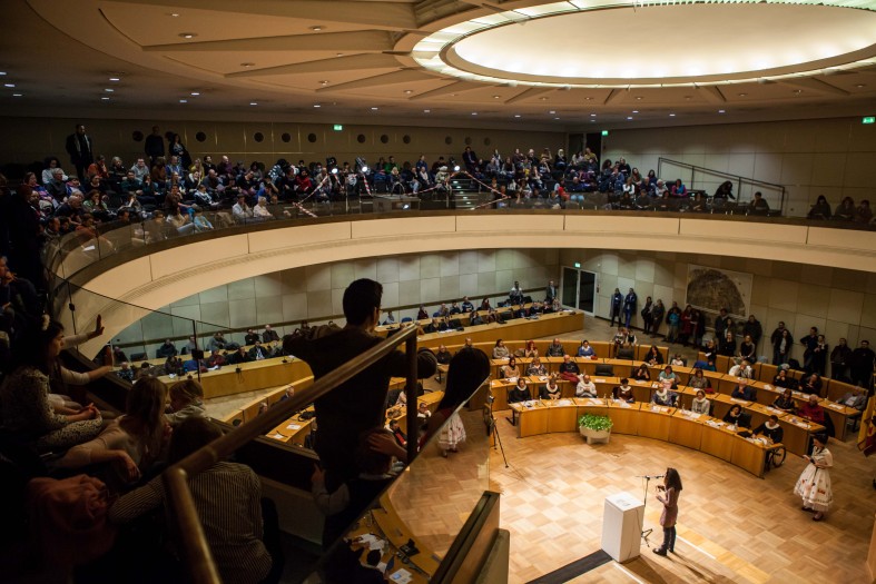 Vielen Menschen sitzen in einem großen Saal, hören zu