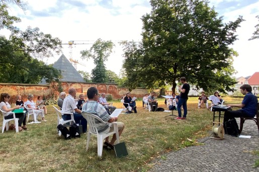 Mehrere Personen sitzen mit Abstand auf weißen Plastikstühlen im Halbkreis