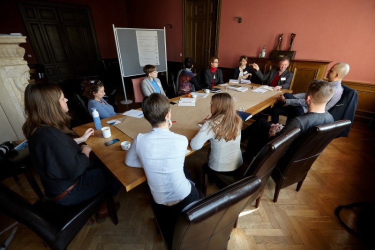 Verschiedene Menschen sitzen an Tisch, unterhalten sich