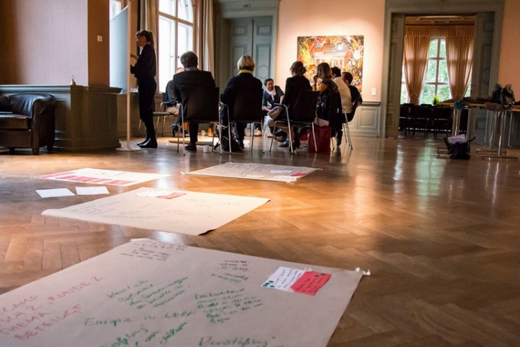 Verschiedene Menschen bei Konferenz, im Vordergrund Arbeitspapiere