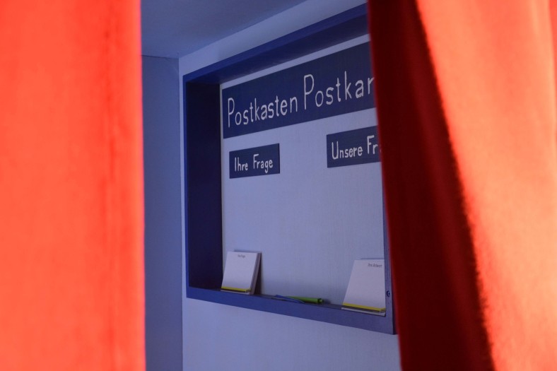 Kasten, innerhalb des Kastens Schild mit Aufschrift "Postkasten - Ihre Frage"