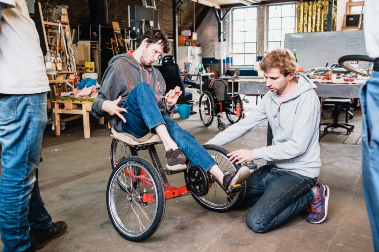 Drei Männer arbeiten in einer Werkstatt am Prototyp eines neuen Rollstuhls. Einer von ihnen sitzt in diesem neuen Rollstuhl.
